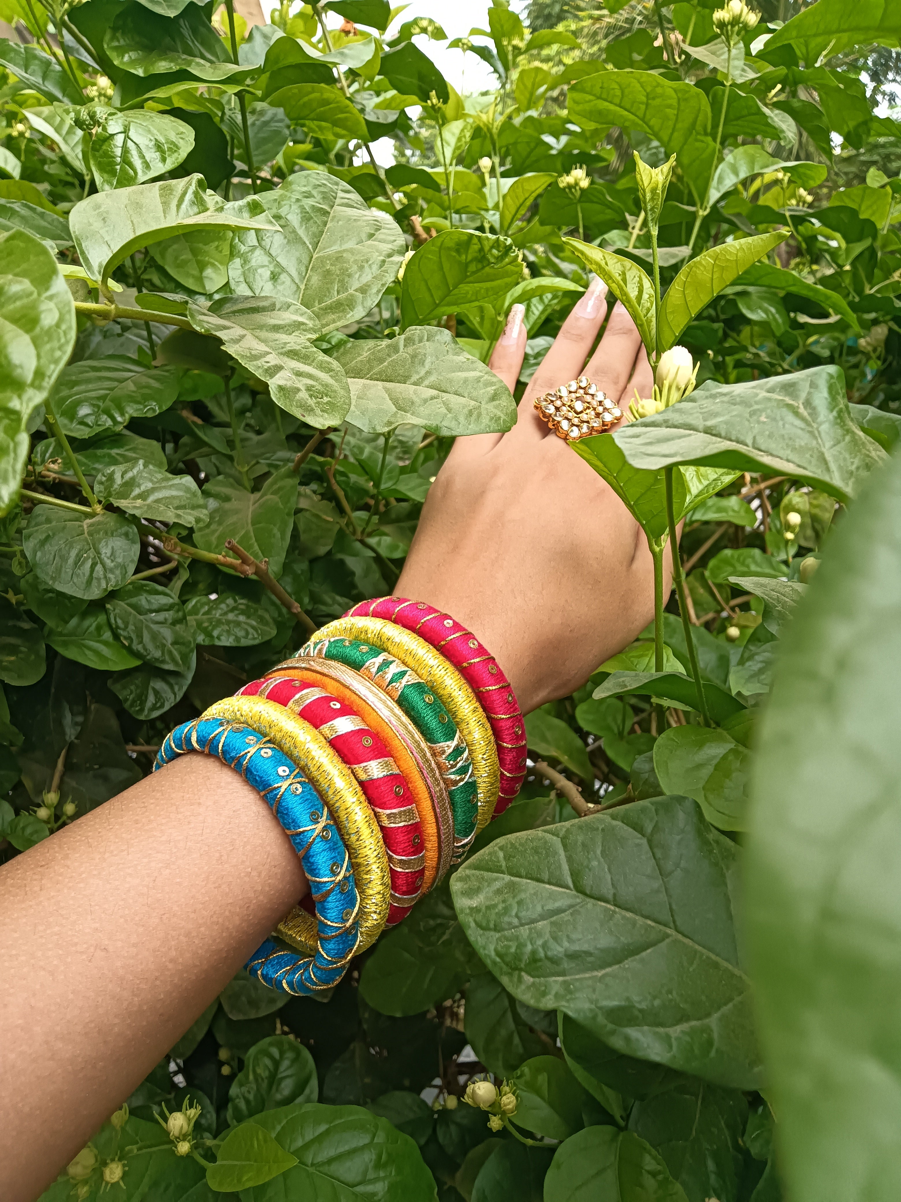Hand wearing colorful bangles with a green leafy background